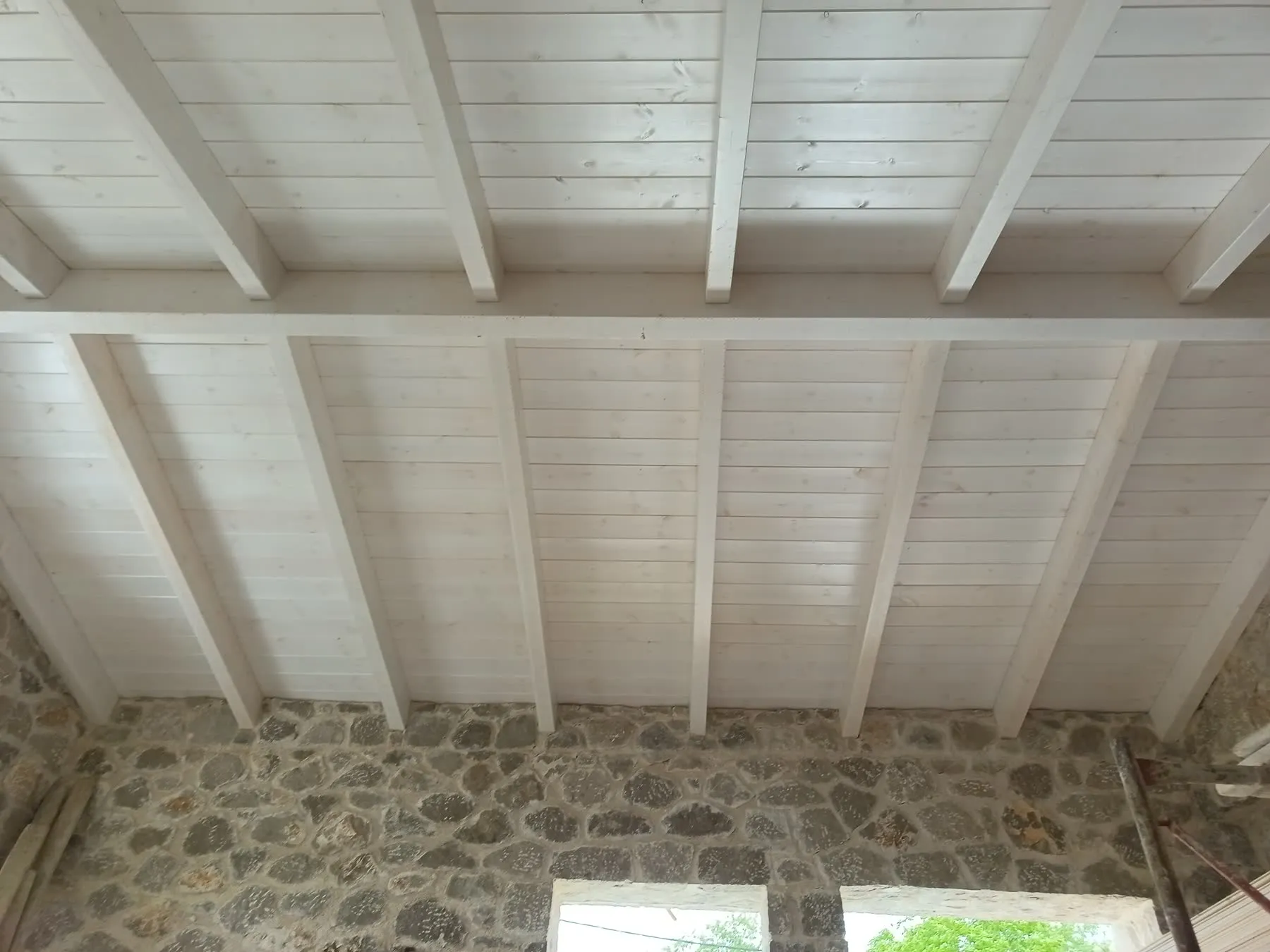 Light-coloured timber beams and ceiling boards seen from inside a stone building
